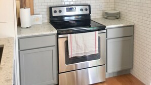 A kitchen with white subway tiles, stainless steel appliances, grey cabinets, and a wooden countertop.