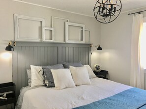 A neatly made bed with white and gray bedding, a headboard with decorative frames, bedside lamps, and a ceiling fan. - Centrally Located Home With Self Check-In (Lincoln)