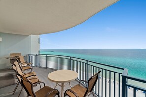 Ein Balkon mit Tisch und Stühlen mit Blick auf einen Strand und den Ozean.