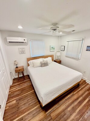 A bedroom with a bed, a ceiling fan, an air conditioner, and two bedside tables.