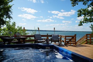 Eine Holzterrasse mit Whirlpool, Liegestühlen und einem Tisch mit Flasche und Glas.