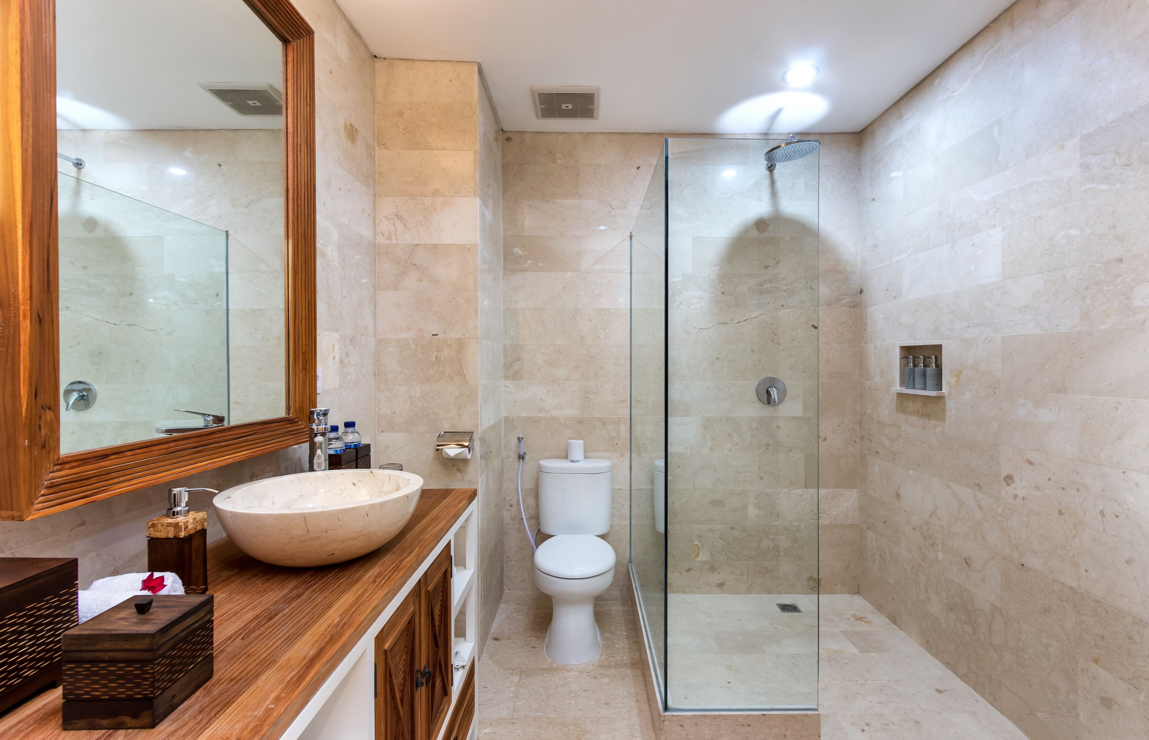 Un baño moderno con un mueble de tocador de madera grande, un lavabo blanco, una cabina de ducha de vidrio y un inodoro.