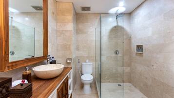 Un baño moderno con un mueble de tocador de madera grande, un lavabo blanco, una cabina de ducha de vidrio y un inodoro.