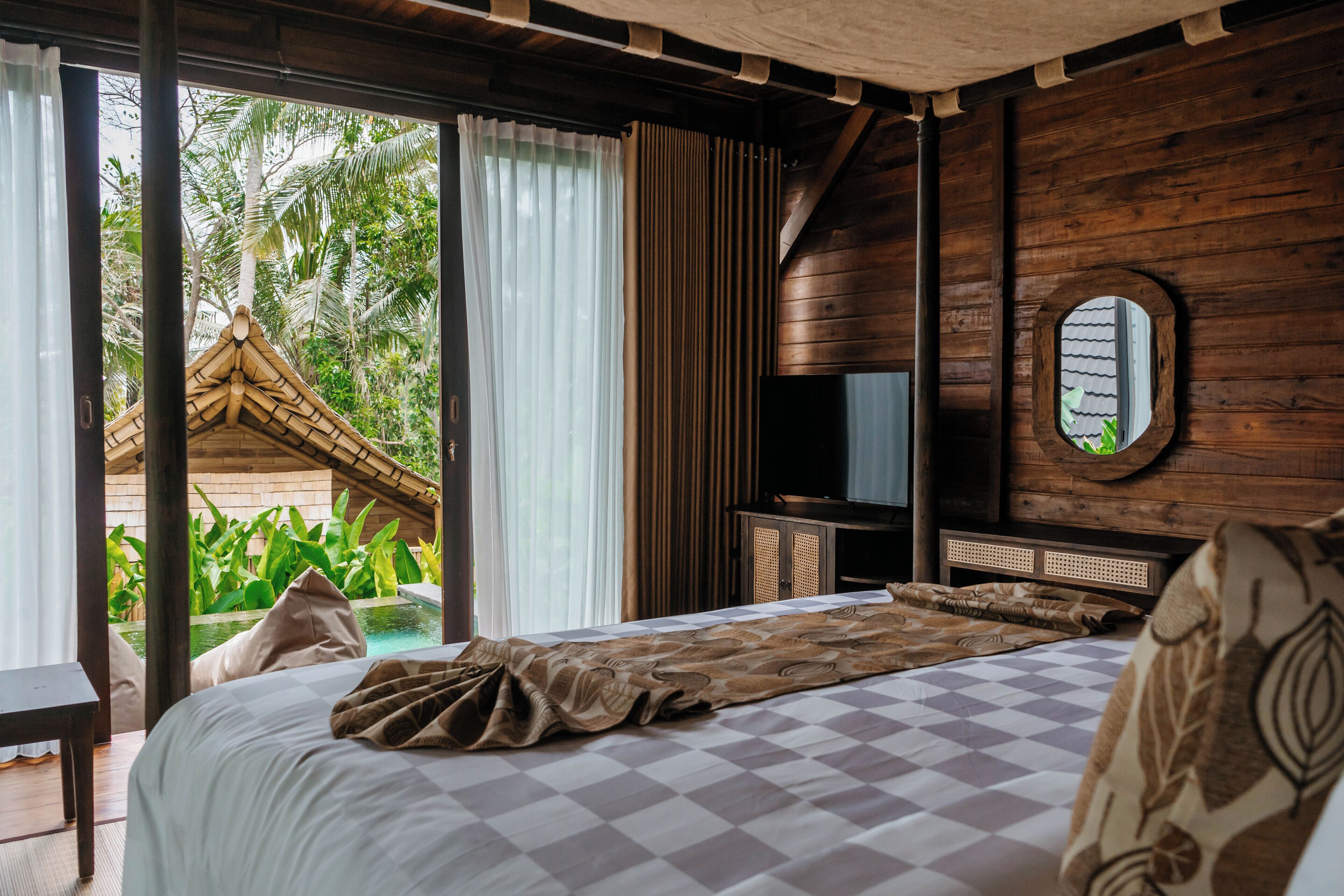 A bedroom with a checkered bedspread, a television on a wooden cabinet, and a view of a palm tree outside.