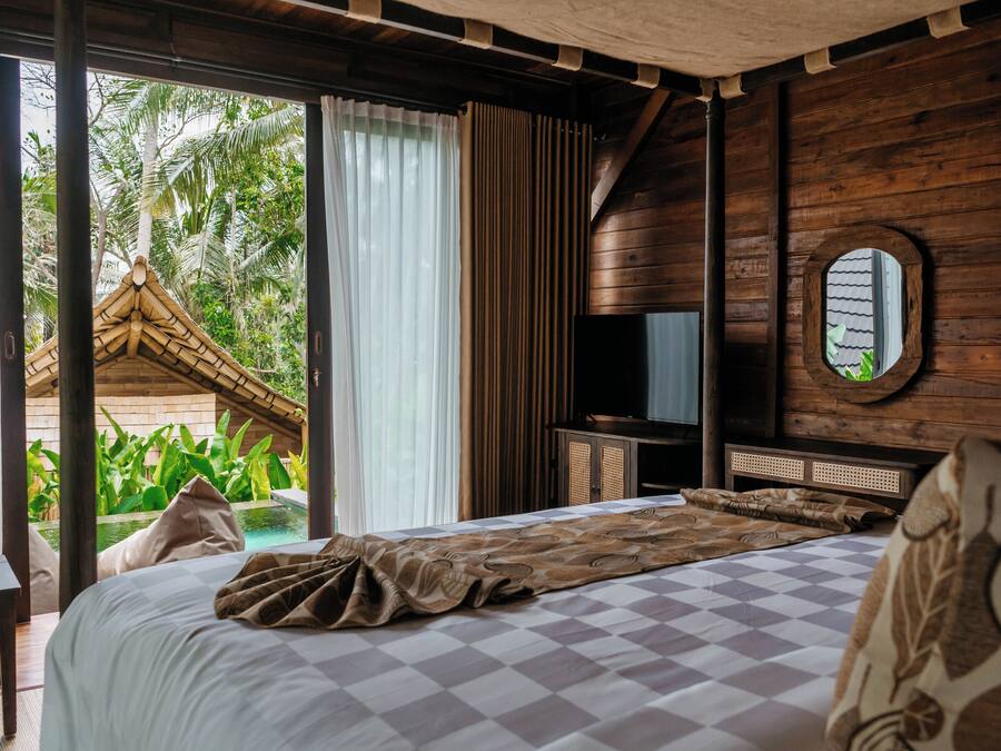 A bedroom with a checkered bedspread, a television on a wooden cabinet, and a view of a palm tree outside.