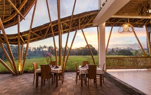 A bamboo structure with a dining area, tables, chairs, and a view of a landscape. - Wadari Retreat Villa Ubud (Ubud)