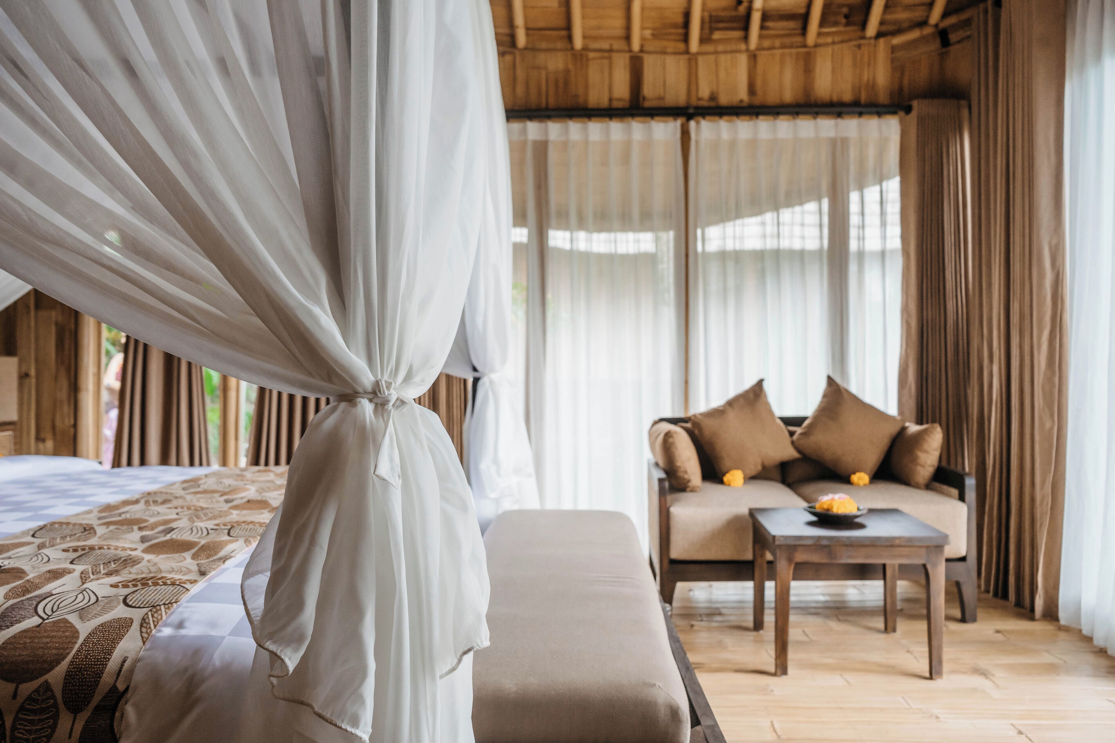 A bedroom with a canopy bed, a sofa with cushions, a small table with fruit, and a wooden floor.