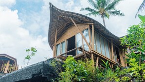 A bamboo structure with a curved roof, large windows, and surrounded by tropical vegetation. - Wadari Retreat Villa Ubud (Ubud)