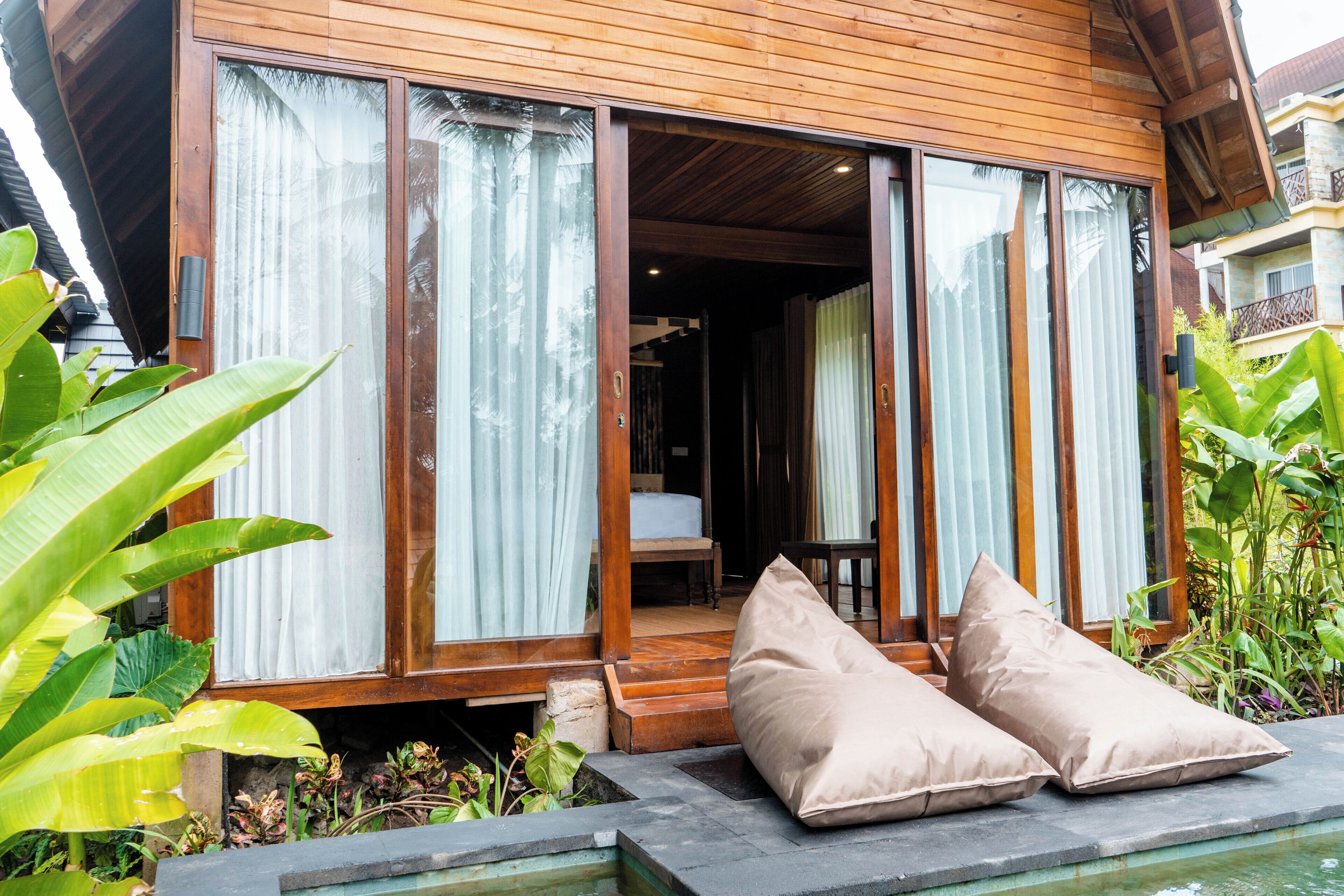 A wooden house with large sliding glass doors, a small porch with cushions, and a stone pathway leading to the entrance.