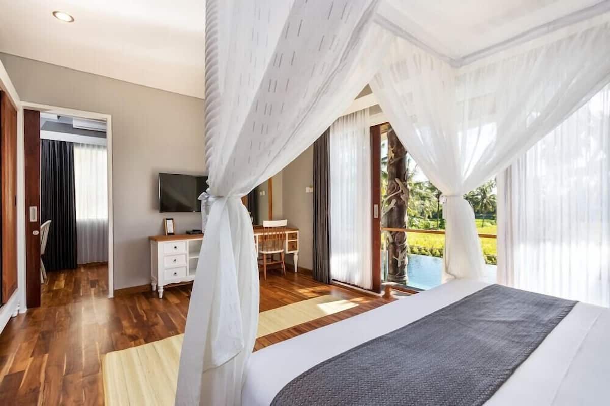 Un dormitorio con cama, televisor, escritorio y vistas al exterior.