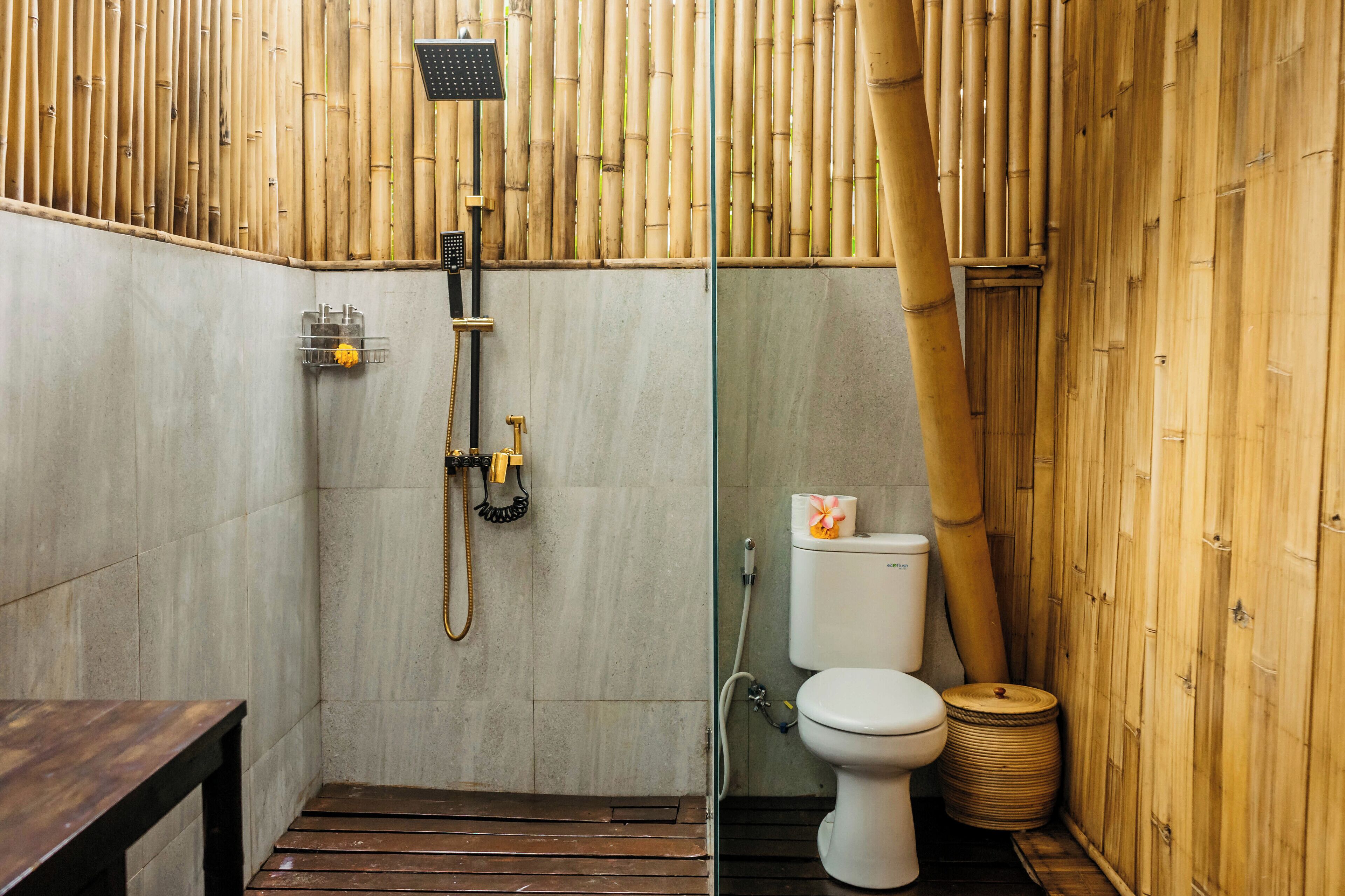 A bathroom with a bamboo wall, a shower, a toilet, and a wooden bench.