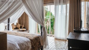 A bedroom with a canopy bed, a wooden floor, a nightstand, and a view of greenery outside. - Wadari Retreat Villa Ubud (Ubud)
