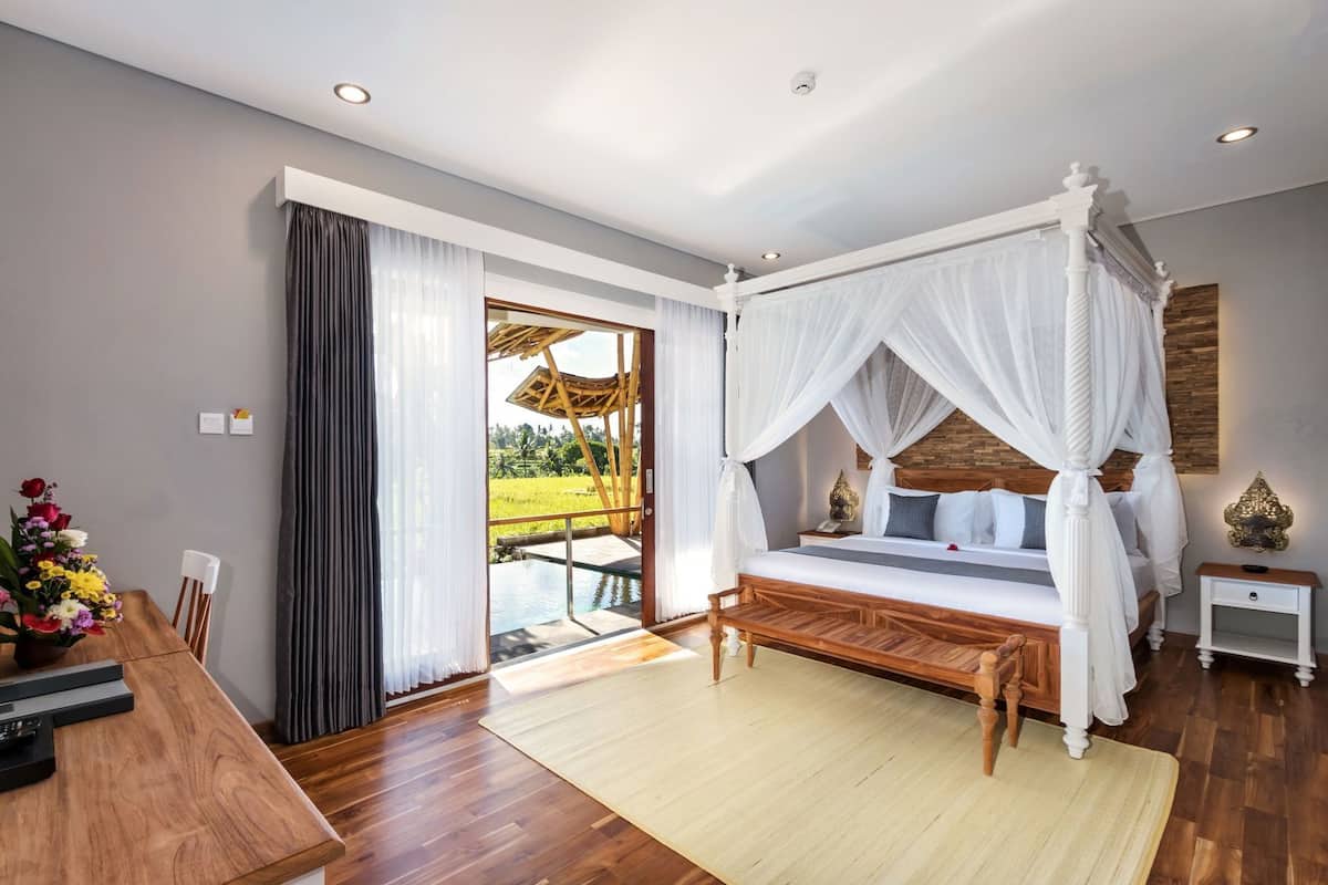Un dormitorio con cama con dosel, un escritorio de madera, una mesa de comedor y vistas a una piscina y jardín.