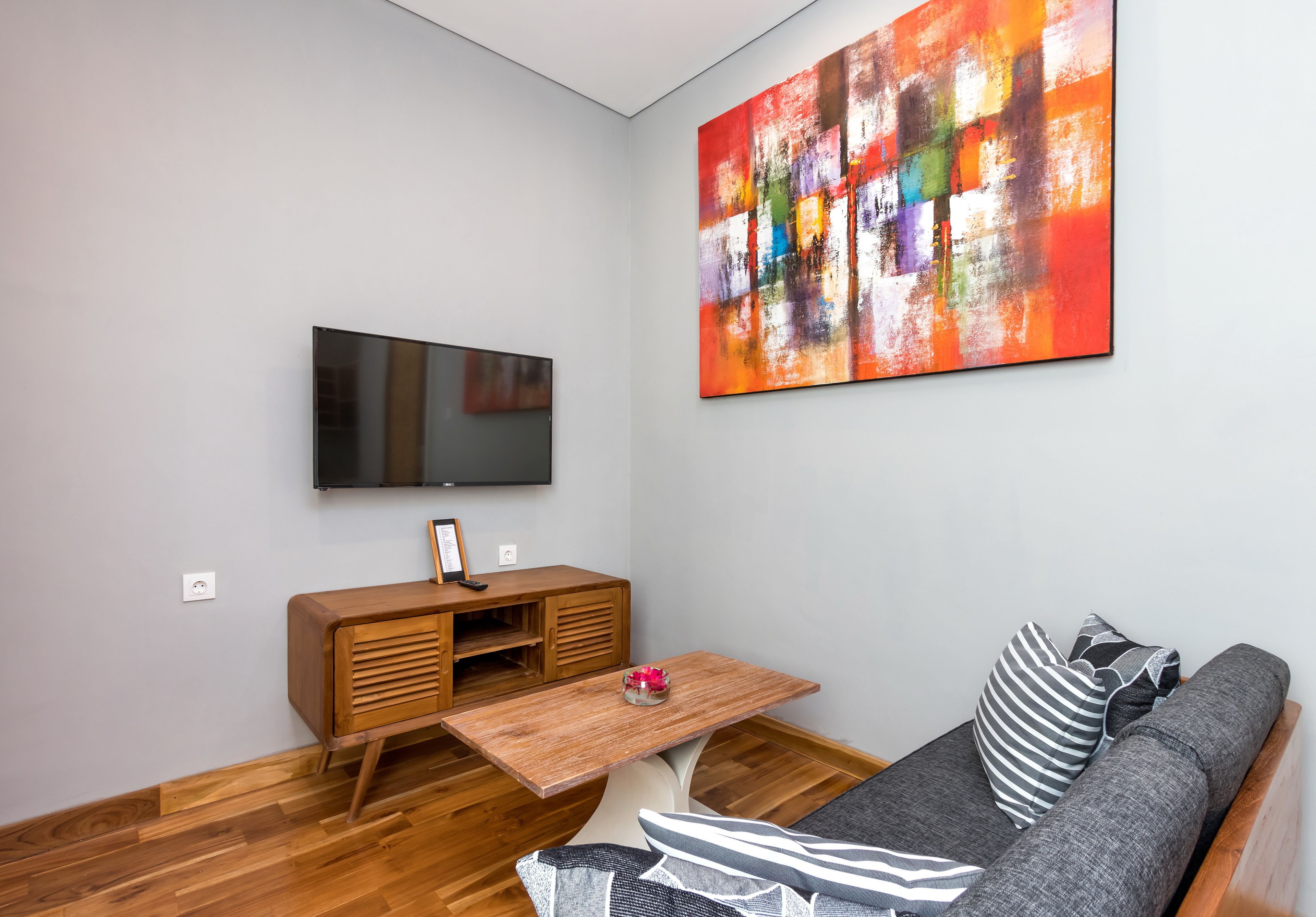 A modern living room with a flat-screen TV, a wooden entertainment unit, a coffee table, and a gray sofa with striped pillows.