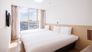 Une chambre d’hôtel avec un grand lit, une tête de lit en bois, une vue sur la ville et une fenêtre avec des rideaux.