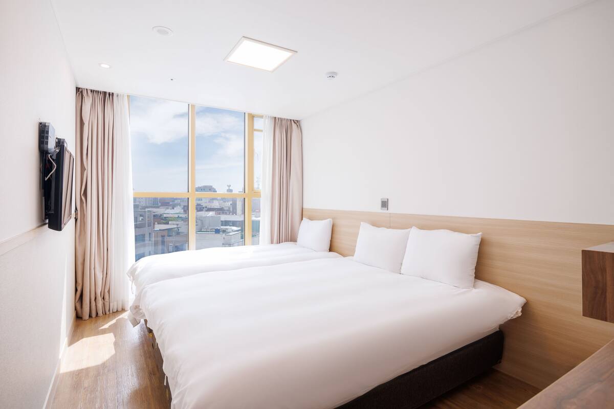 Een hotelkamer met een groot bed, een houten hoofdeinde, uitzicht op de stad en een raam met gordijnen.