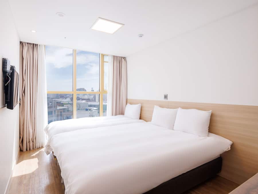 Een hotelkamer met een groot bed, een houten hoofdeinde, uitzicht op de stad en een raam met gordijnen.