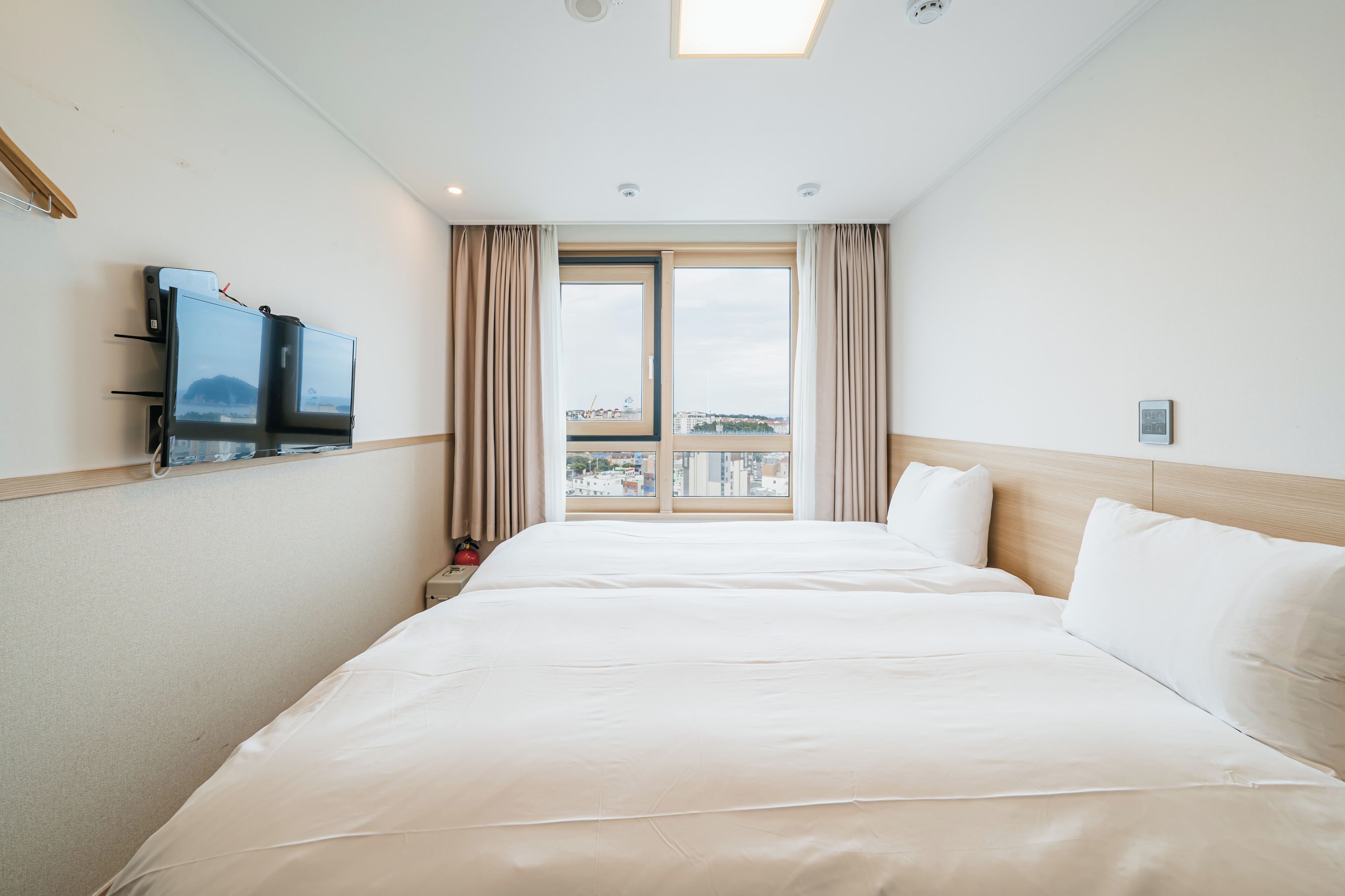 A hotel room with a large bed, a TV mounted on the wall, and a window with curtains.