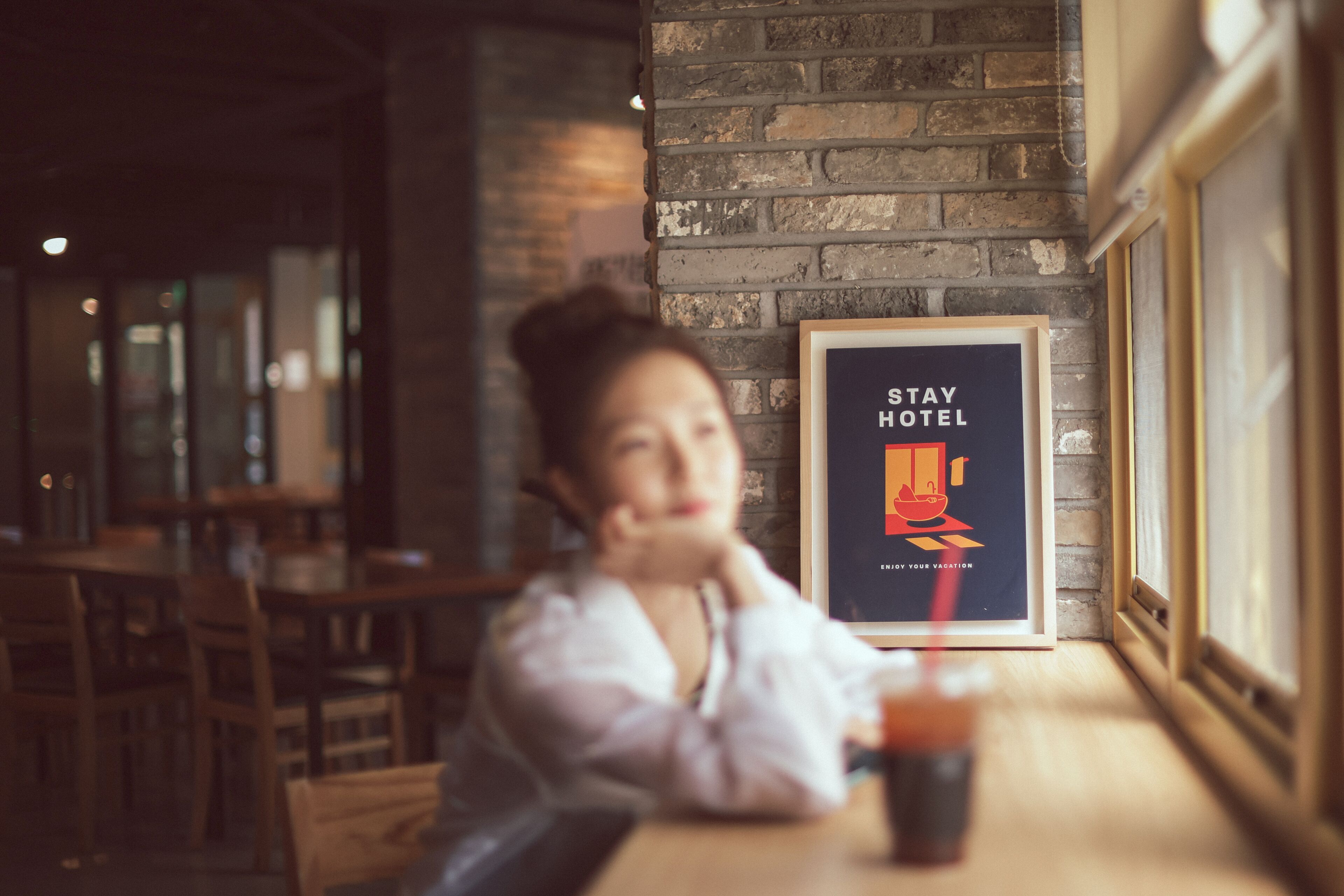 A person sitting at a table in a restaurant with a framed poster on the wall that reads "STAY HOTEL."