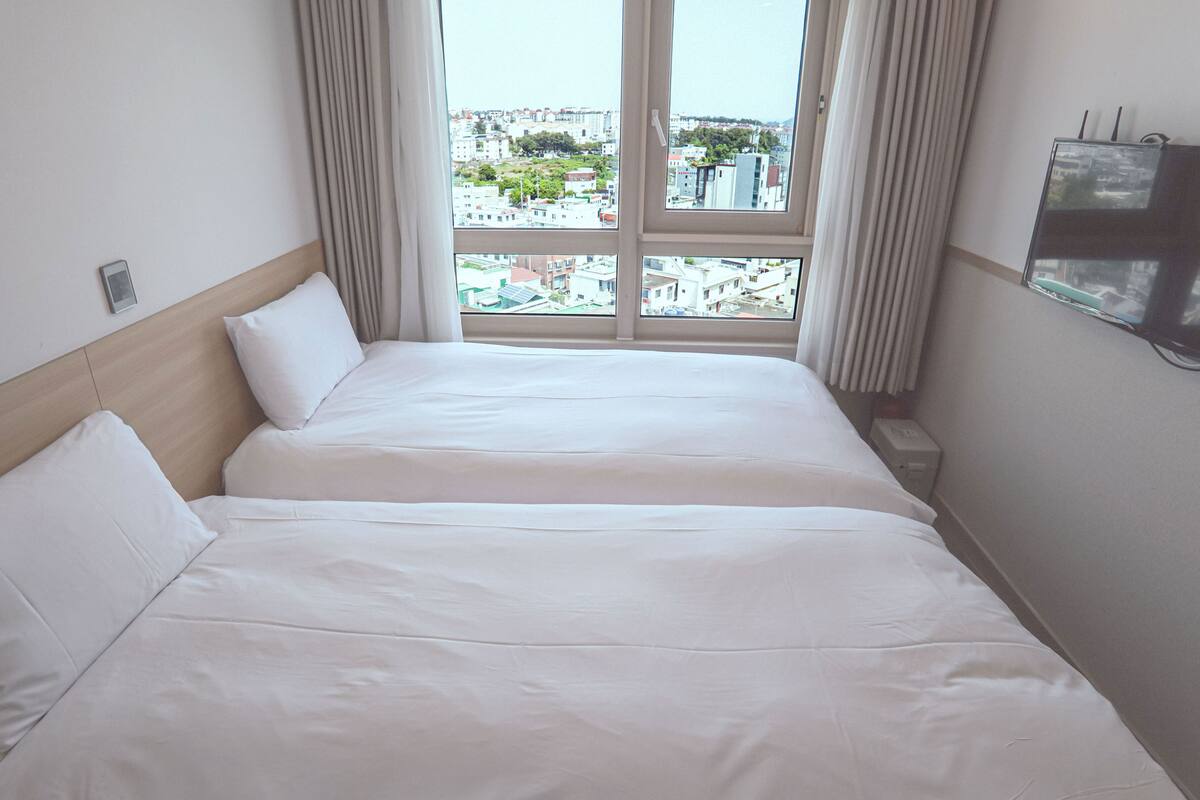 Een hotelkamer met twee bedden, een groot raam met gordijnen en een televisie aan de muur.