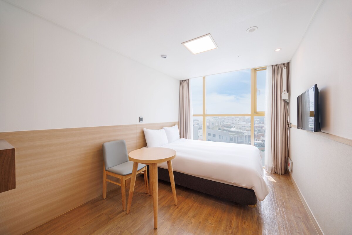 Een hotelkamer met een groot bed, een kleine tafel, een stoel, een televisie en een raam met gordijnen.