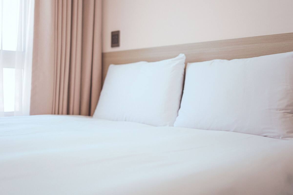 Een net opgemaakt bed met witte lakens en een houten hoofdeinde.