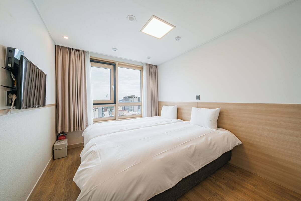 Hotelkamer met een groot bed, een aan de muur bevestigde televisie, een raam met gordijnen en uitzicht op de stad.