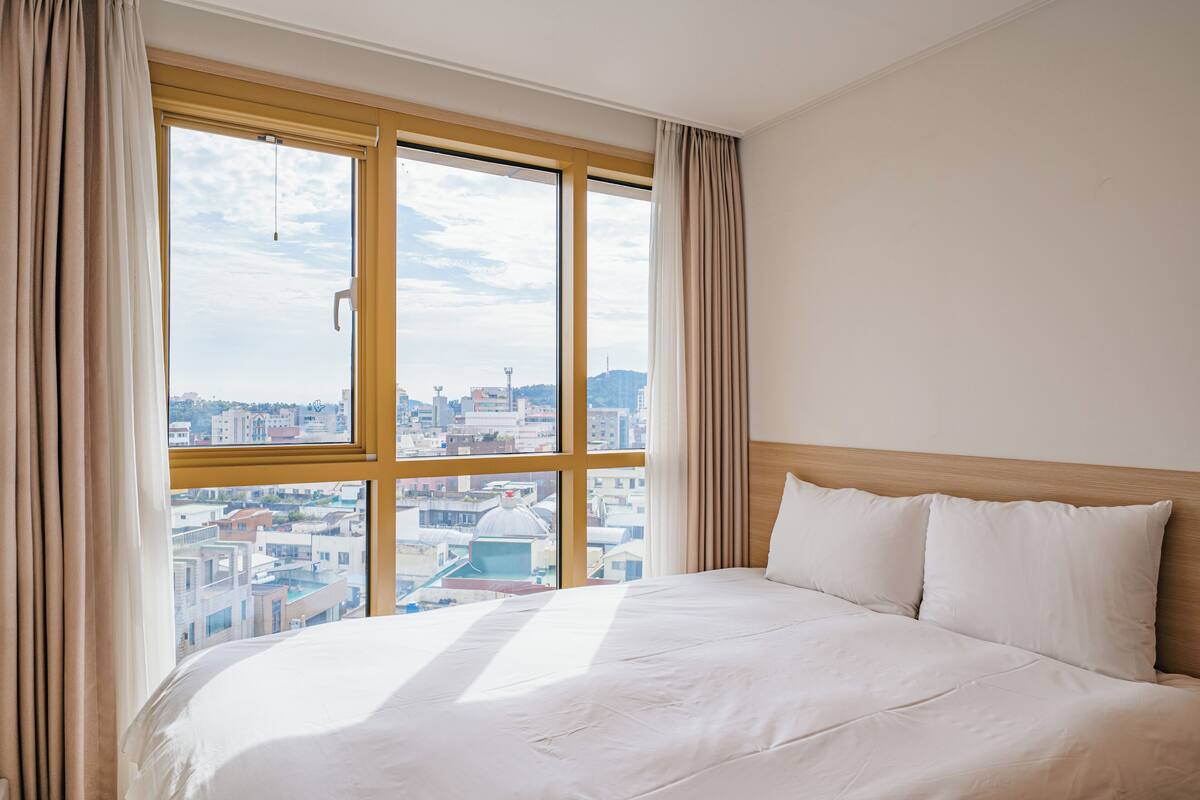 Een hotelkamer met een groot raam, een bed en gordijnen.