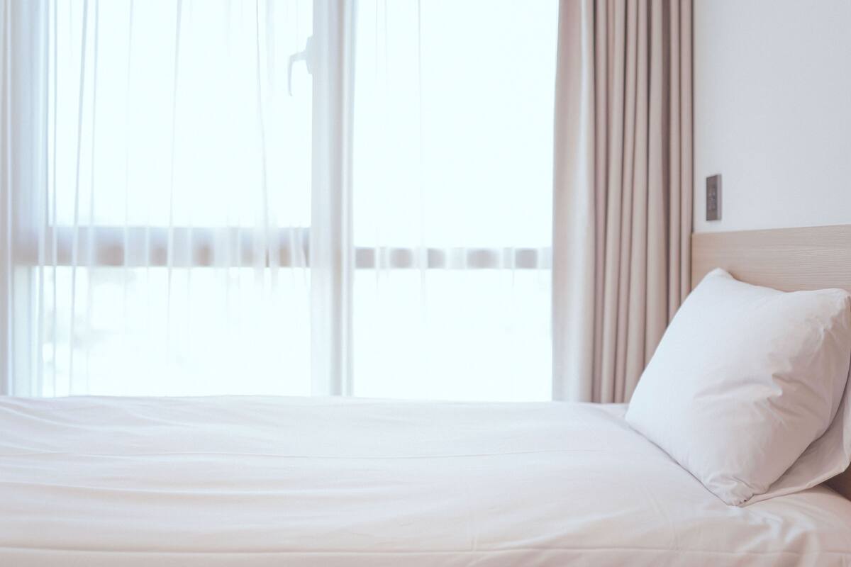 Een hotelkamer met een bed, gordijnen en uitzicht door het raam.
