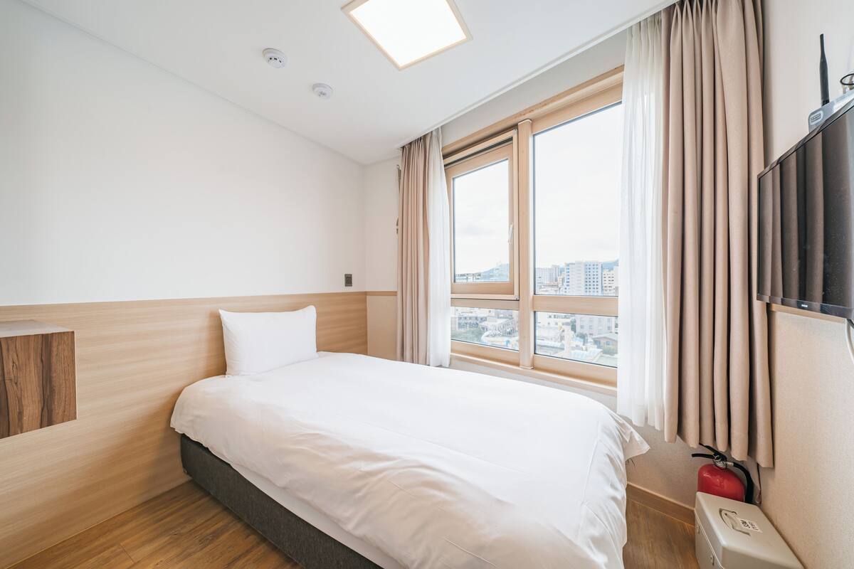 Hotelkamer met een groot bed, een raam met gordijnen, een flatscreen televisie aan de muur en een brandblusser.