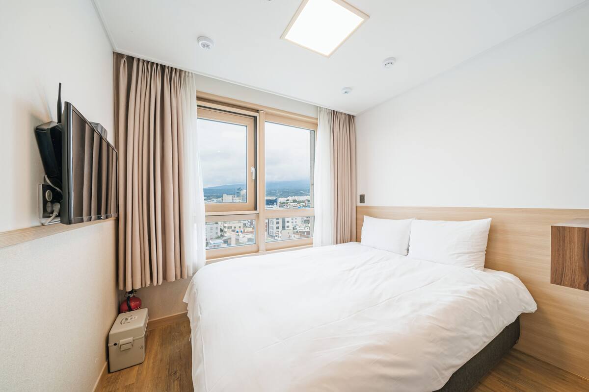 Een hotelkamer met een groot bed, een televisie aan de muur en een raam met gordijnen.