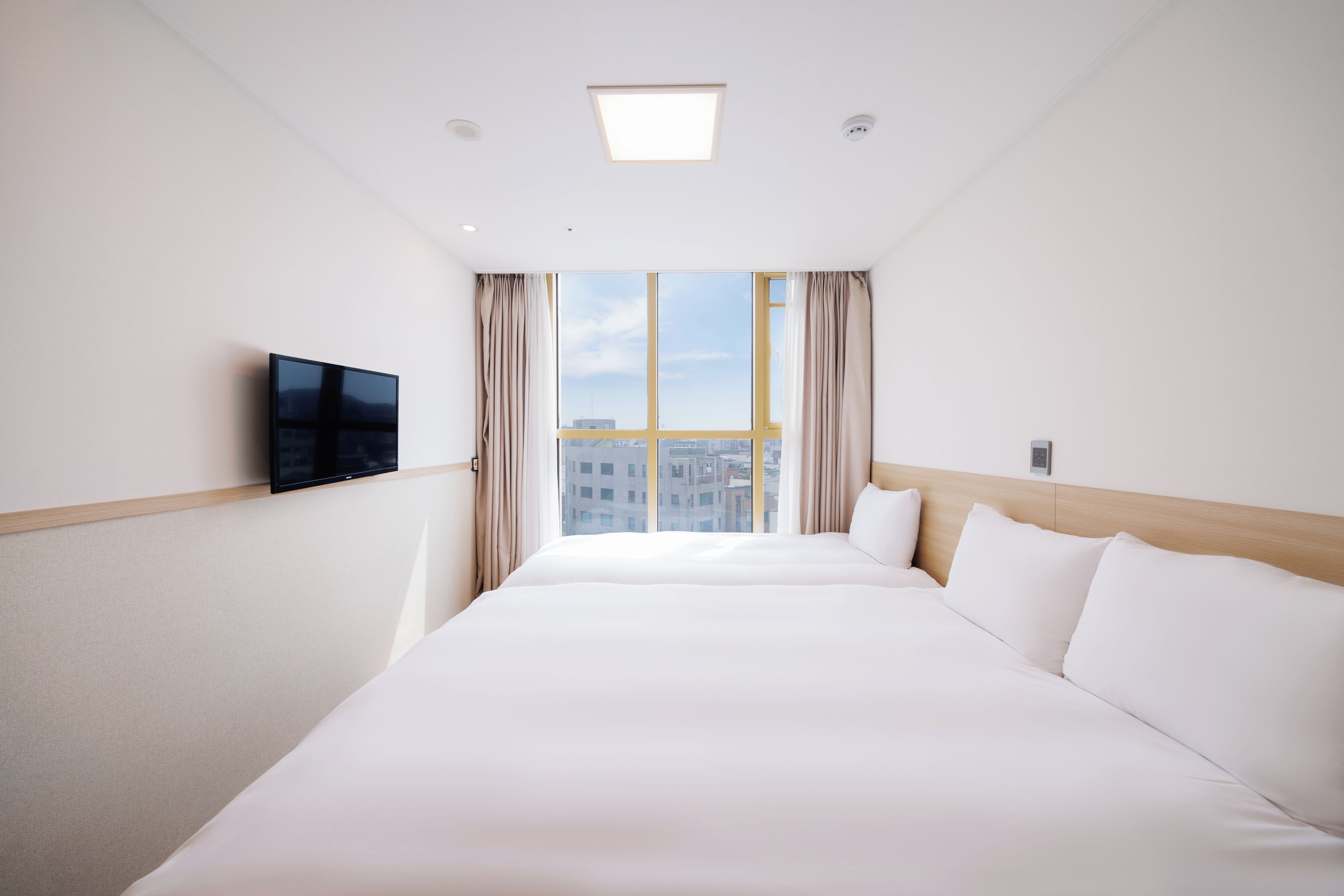 Quarto de hotel com cama grande, televisão de tela plana na parede e janela com cortinas.