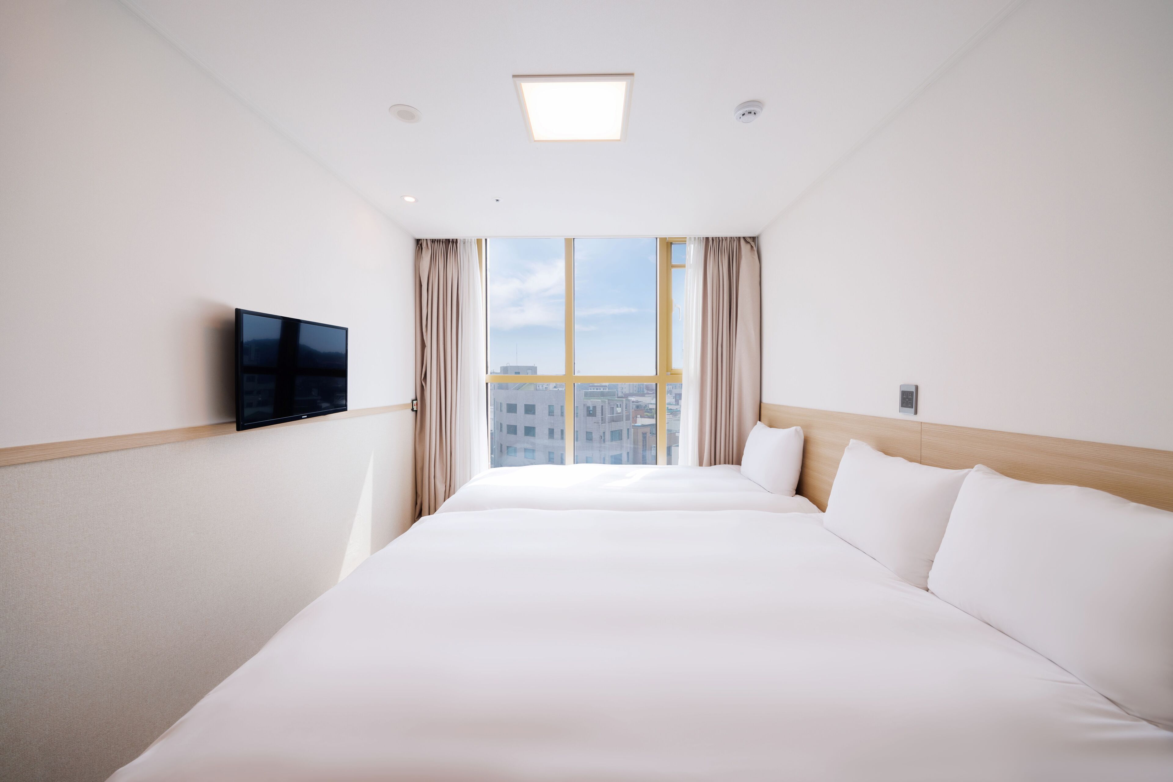 Ein Hotelzimmer mit einem großen Bett, einem flachbildfernseher an der Wand und einem Fenster mit Vorhängen.