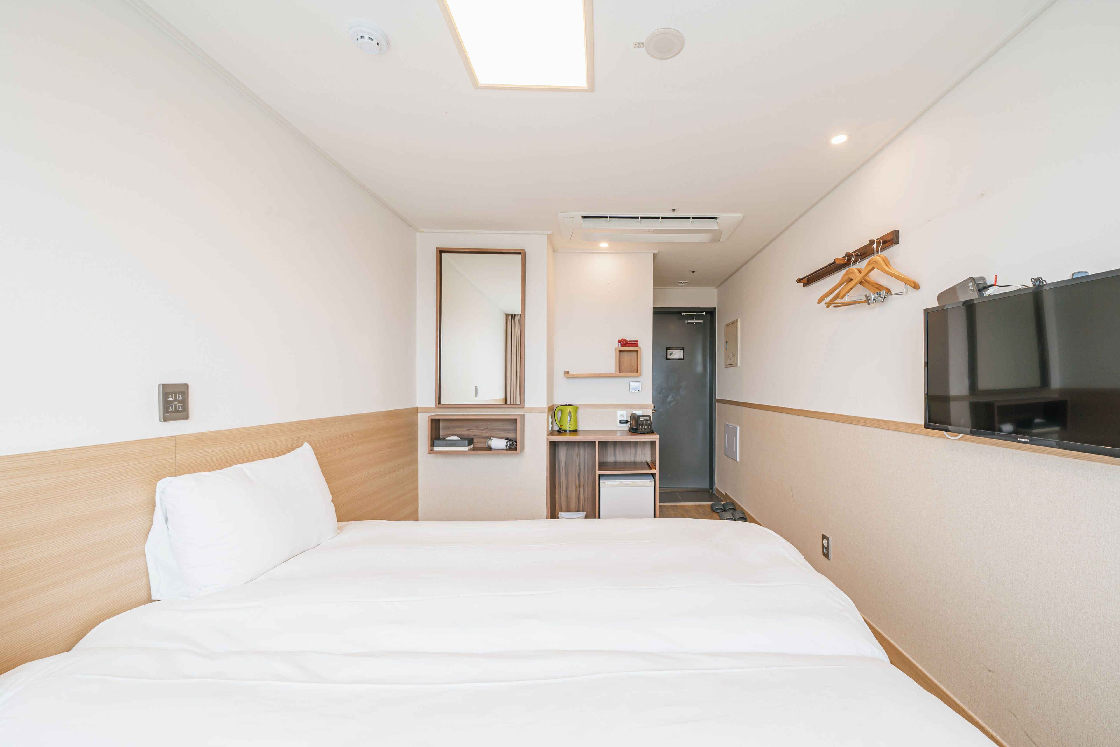 Quarto de hotel com uma cama grande, uma secretária pequena, um espelho, uma televisão e um guarda-roupa.