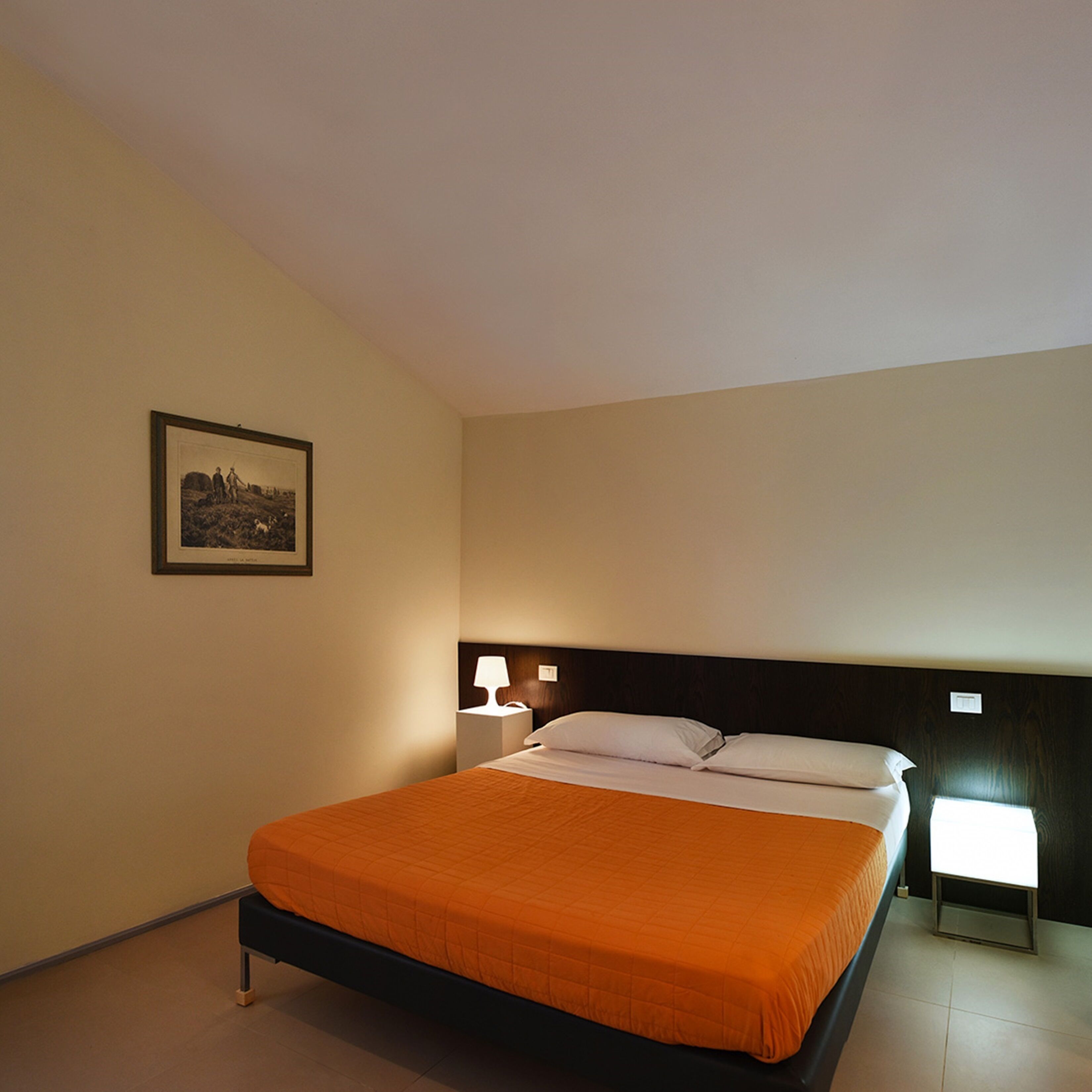 Ein Hotelzimmer mit einem Einzelbett, einem Nachttisch, einer Lampe und einem gerahmten Bild an der Wand.
