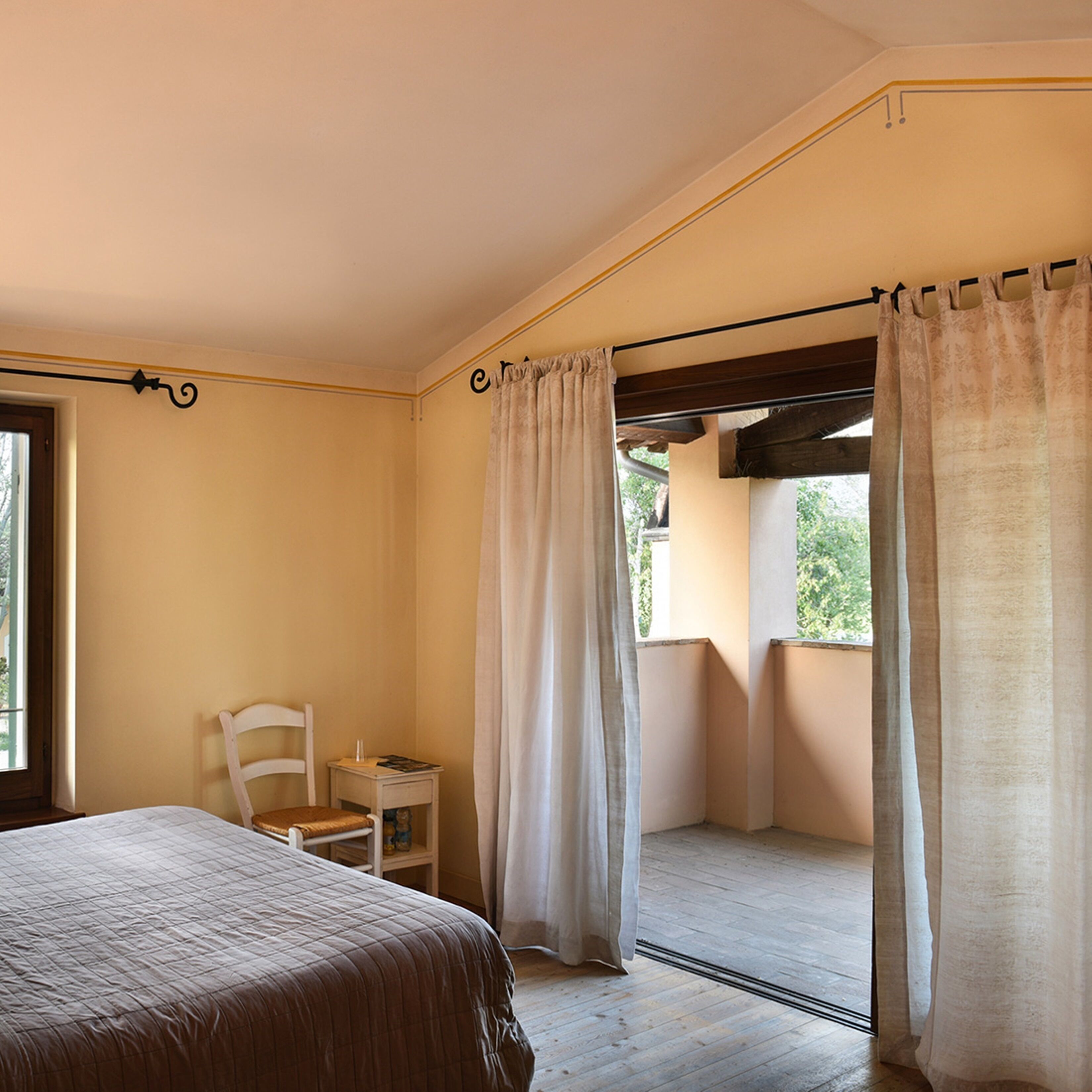 Ein Schlafzimmer mit Bett, einem Sessel, einem kleinen Tisch und einem Fenster mit Vorhängen.