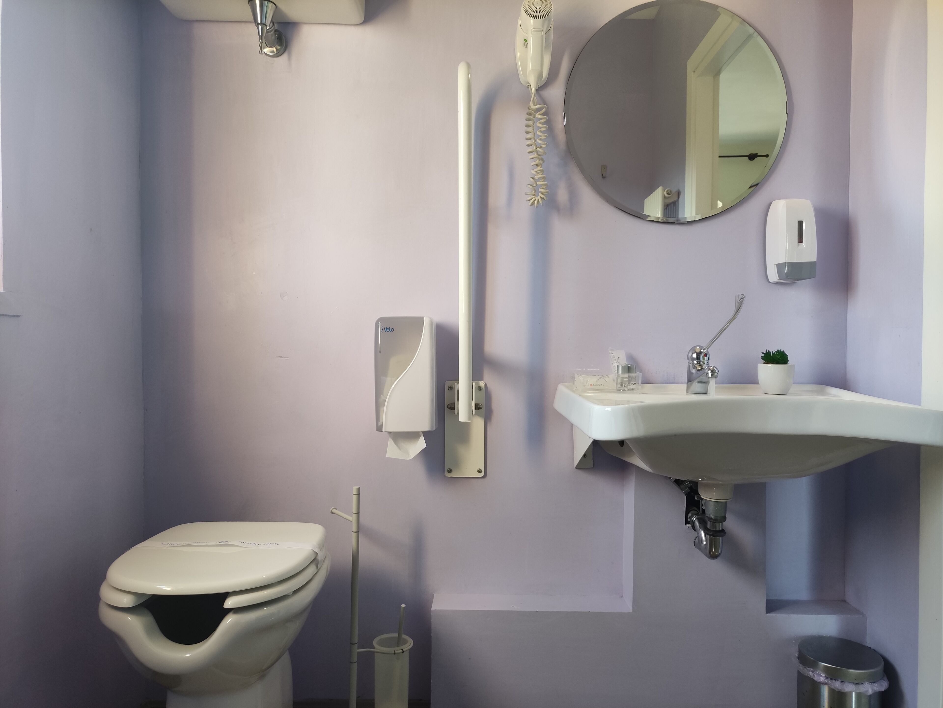 Un baño con inodoro, lavamanos, espejo, secador de pelo y secador de manos.