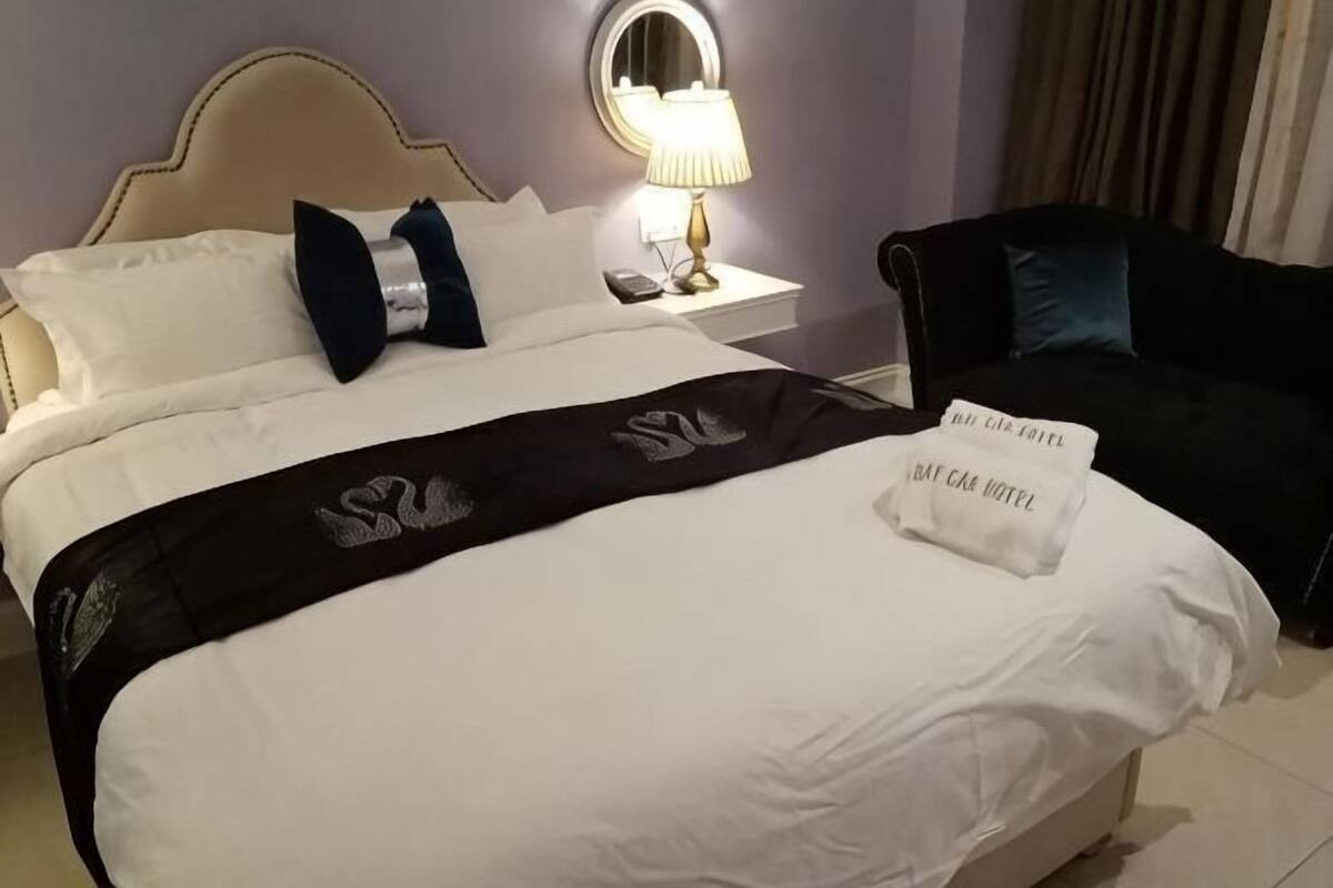A hotel room with a bed, a nightstand, a lamp, and a black sofa.