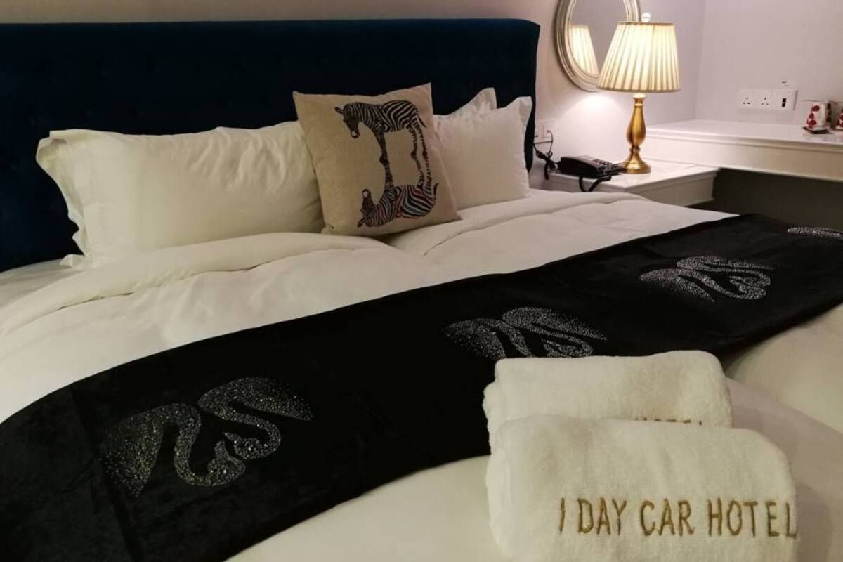 A neatly made bed with white linens, a zebra-themed pillow, a black throw blanket with a logo, and a white towel with text.