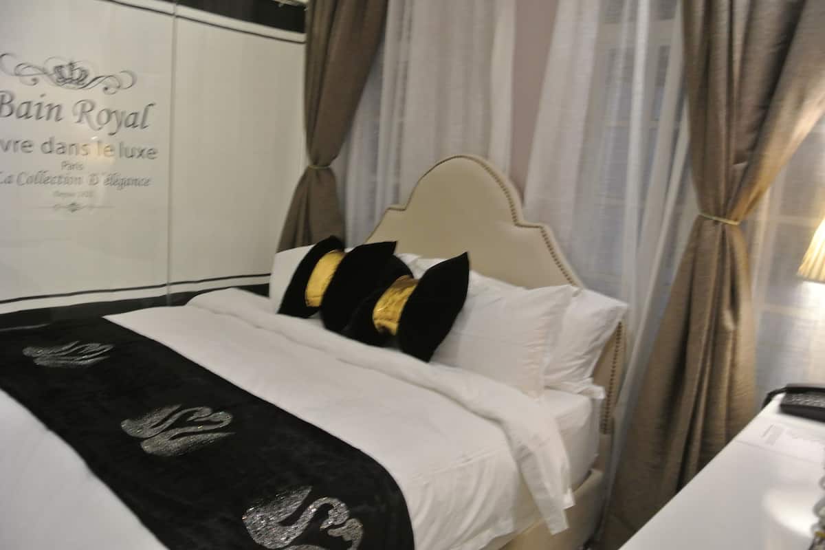 A hotel room with a bed, white bedding, a black and white throw, and a curtain.