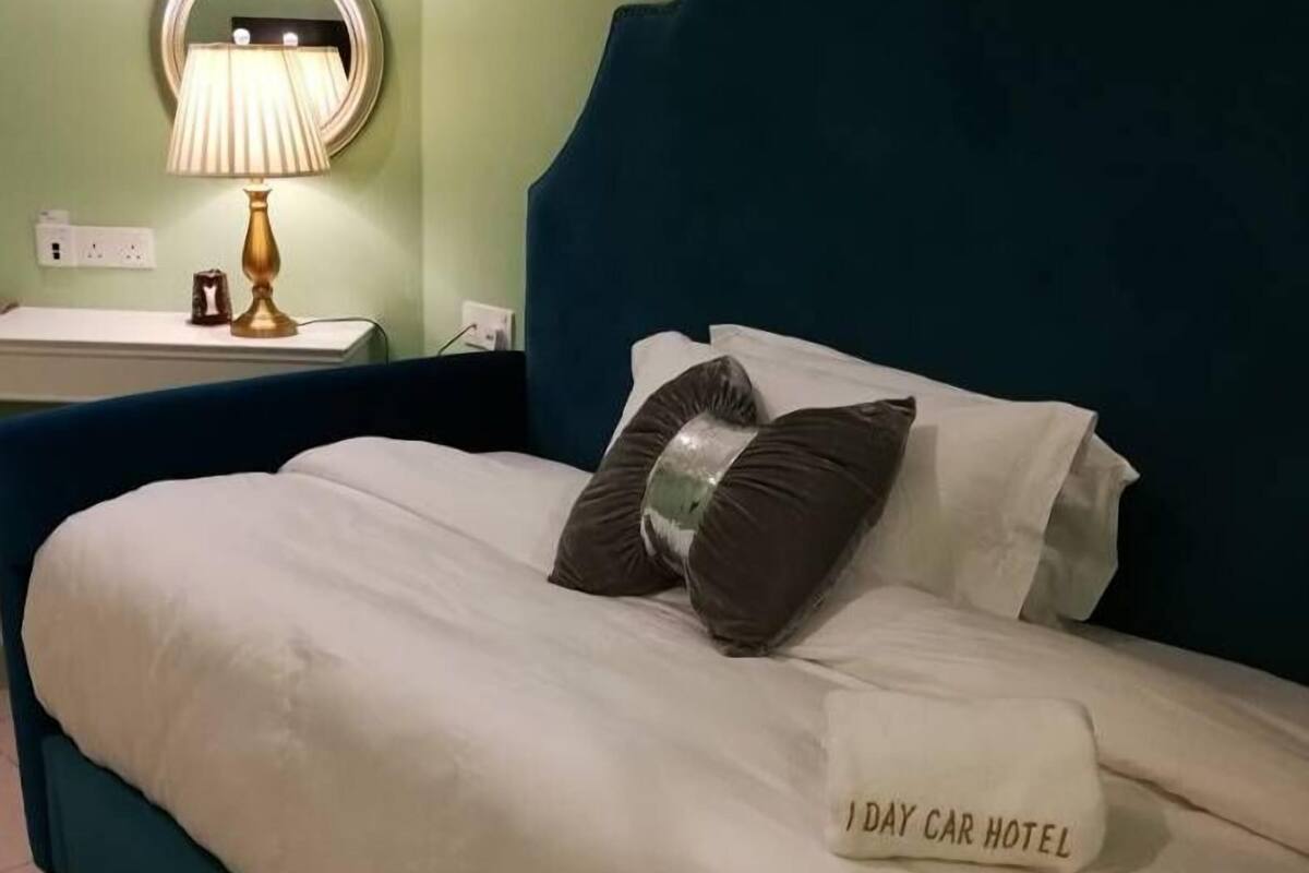 A neatly made bed with a pillow labeled "DAY CAR HOTEL" and a bedside lamp on a nightstand.