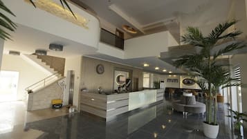 A spacious lobby with a reception desk, a staircase, and a seating area with a large potted plant.