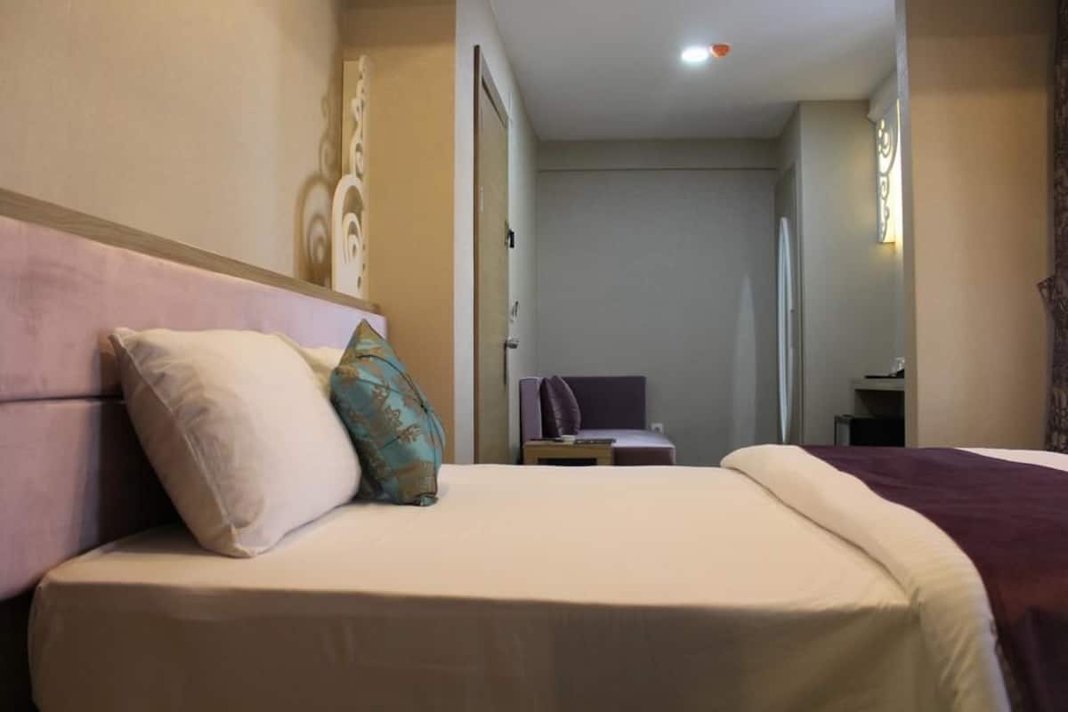 Una habitación de hotel con una cama grande, una mesita de noche y una puerta que conduce a otra habitación.