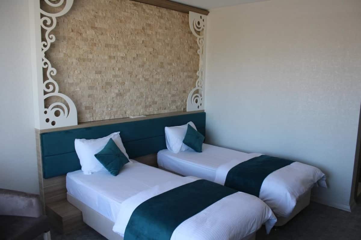 Una habitación de hotel con dos camas, cabecera, paneles decorativos en la pared y un banco.