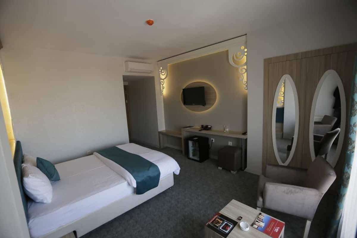Una habitación de hotel con cama, escritorio, silla, espejo y televisión.