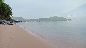 Una playa con mar tranquilo, un muelle y montañas al fondo.