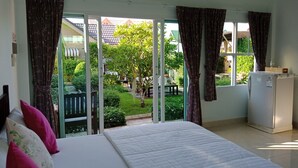 Un dormitorio con cama, refrigerador y vistas a un jardín y casas a través de amplios ventanales.