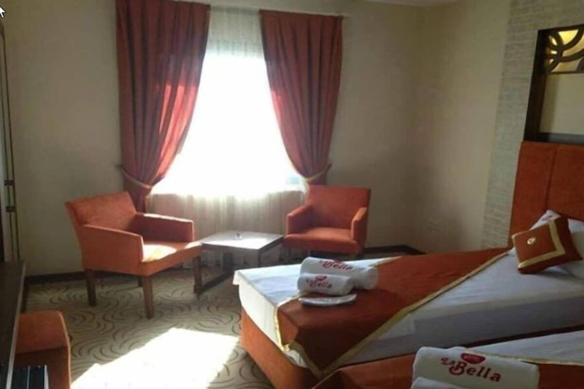 A hotel room with a bed, a chair, a small table, and curtains.