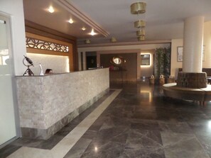 A spacious lobby with a reception desk, a large column, and a round seating area.
