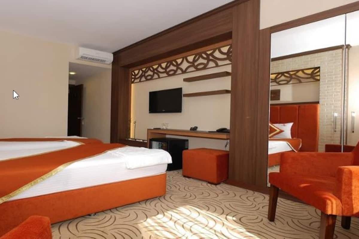A hotel room with a large bed, orange chairs, a TV, and a desk.